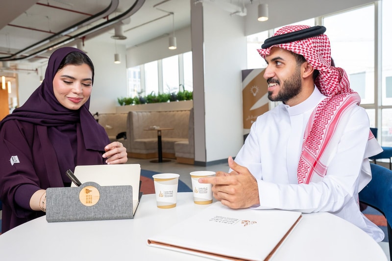 زميلان يتناقشان حول طاولة في بيئة عمل مفتوحة